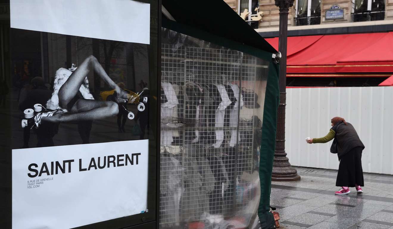 A woman begs on the Champs-Elysees avenue in Paris, next to an advertising poster for the French fashion house Yves Saint Laurent. Photo: AFP