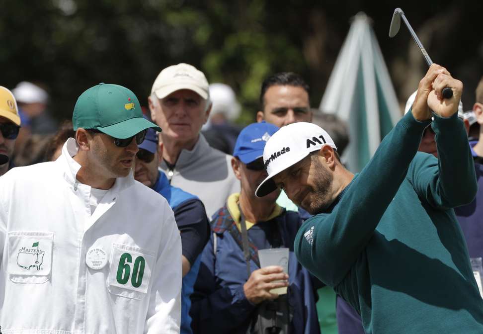 A pained looking Dustin Johnson tests his swing next to his caddie before pulling out of the Masters. Photo: Reuters