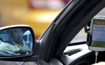 A driver is reflected in a side mirror as he uses the Didi Chuxing car-hailing application. Photo: Reuters