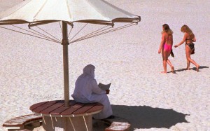 A man reads a newspaper on a Dubai beach, as Western tourists walk by. Photo: AP A man reads a newspaper on a Dubai beach, as Western tourists walk by. Photo: AP