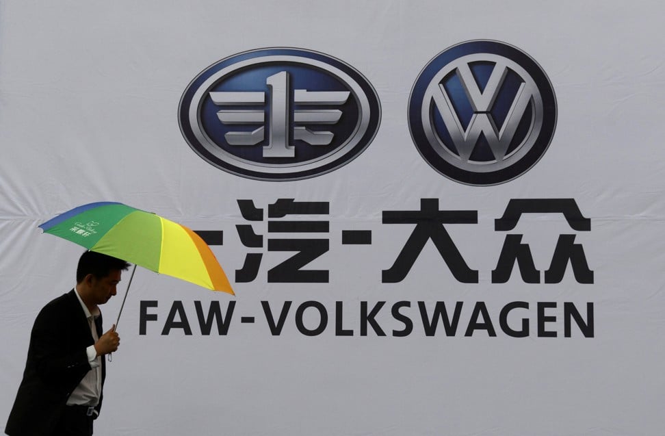 FILE PHOTO: A man holds an umbrella as he walks past a company logo of FAW-Volkswagen at an automobile exhibition in Fuyang, Anhui province, September 12, 2014. Photo: Reuters