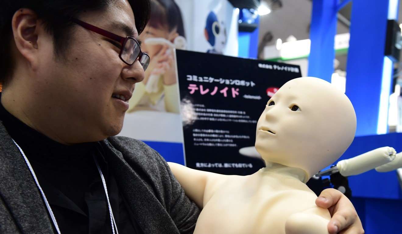 An employee from Japan’s robot venture Telenoid Planning chats with a humanoid robot developed to keep the elderly company. Photo: AFP