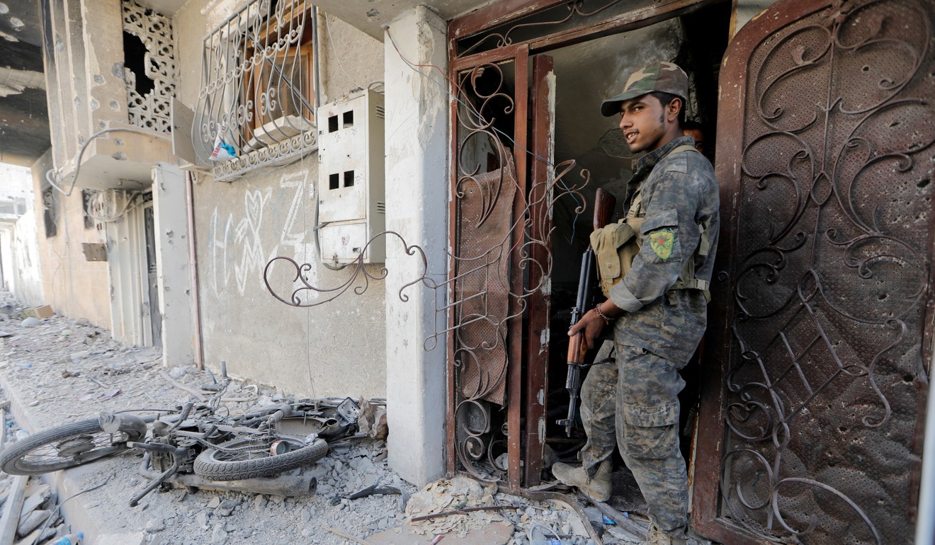 A member of the Syrian Democratic Forces talks to his comrade as he hides from Islamic State's sniper in the old city of Raqqa, Syria. Photo: Reuters