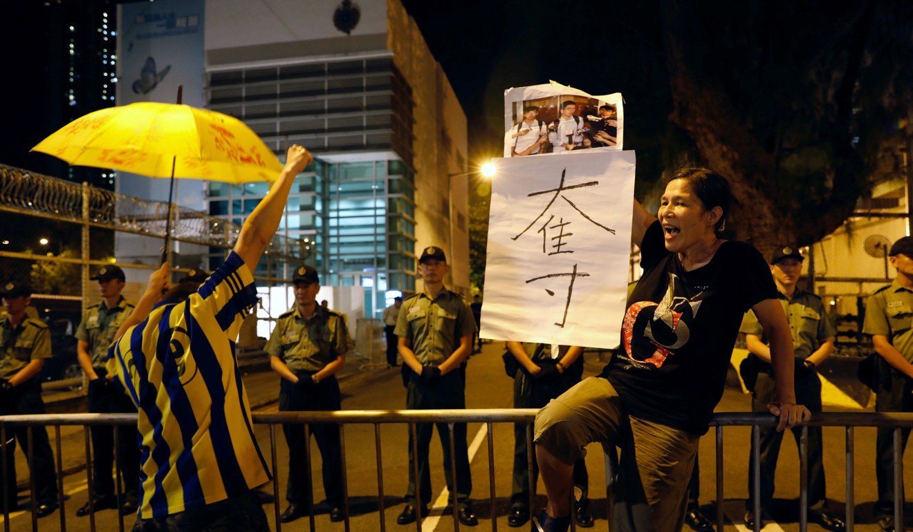 A protester holds a yellow umbrella, the symbol of the Occupy movement, in support of the jailed Hong Kong student leaders, as Correctional Services Department officers stand guard outside the prison, on August 18. Photo: Reuters