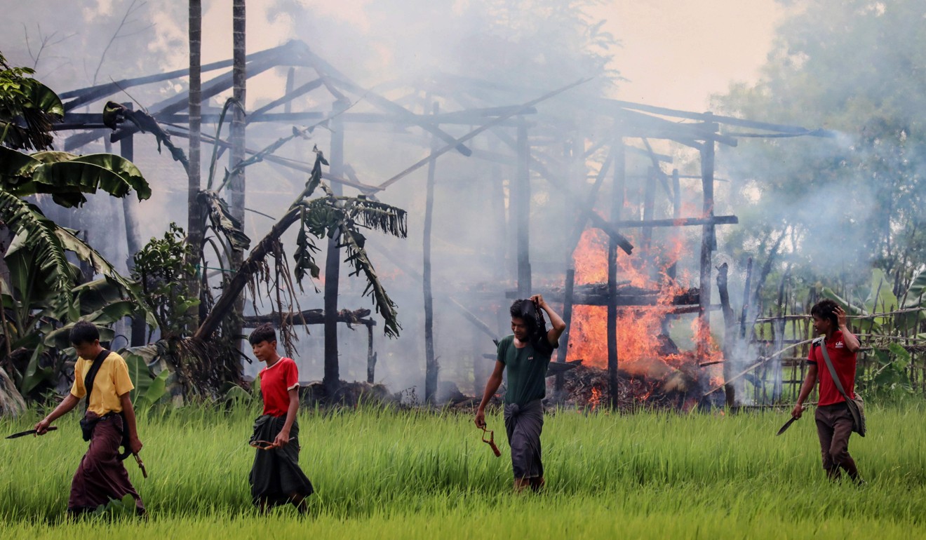 Unidentified men carry knives and slingshots as they walk past a burning house in Gawdu Tharya village near Maungdaw in Rakhine state in northern Myanmar. File photo AFP