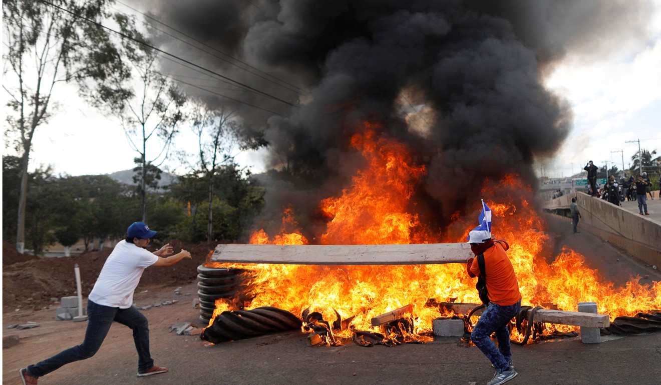 Demonstrators throw a piece of wood onto burning tyres at a barricade. Photo: Reuters