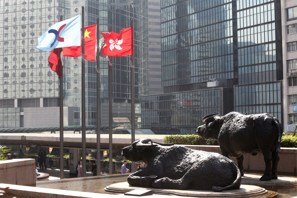 Bronze sculptures of bulls are seen next to the Hong Kong Stock Exchange, China, and Hong Kong flags outside the Hong Kong Stock Exchange in Central, Hong Kong. Photo: SCMP/Dickson Lee