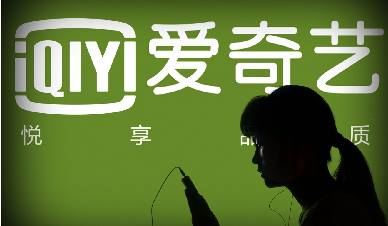 A Chinese woman looks at her mobile phone in front of a logo for the online video sharing site iQiyi. The firm was one of the video companies punished. Photo Imaginechina