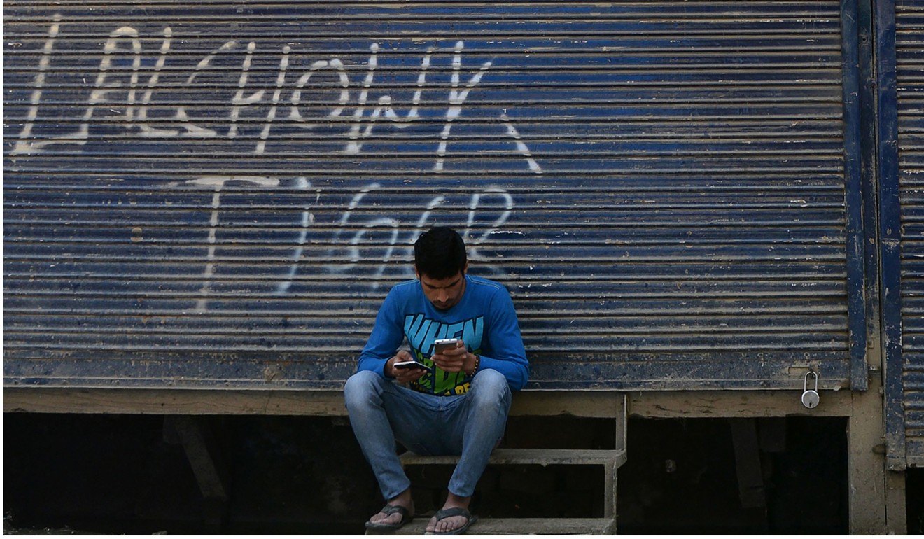 A Kashmiri man looks at his mobile phone in front of closed shops in Srinagar. Photo: AFP