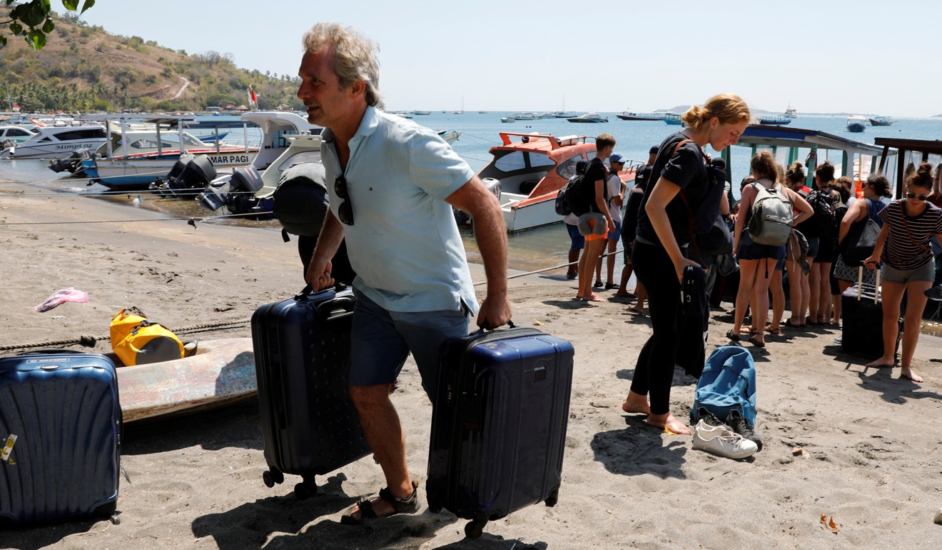 Foreign tourists carry their belongings on the beach as they leave Gili Trawangan island. Photo: Reuters