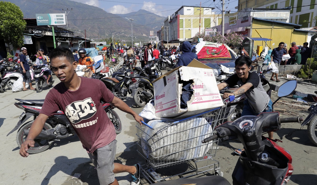 Men drag a shopping trolley with goods from a shopping centre in Palu. Photo: EPA