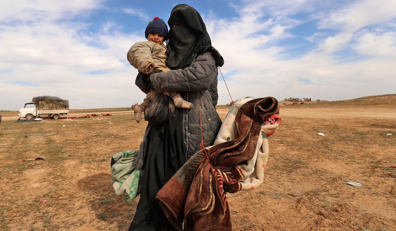 A fully veiled woman holds her baby as civilians fleeing the Islamic State's group embattled holdout of Baghouz walk in a field on February 13, 2019 during an operation by the US-backed Syrian Democratic Forces (SDF) to expel the Islamic State group from the area, in the eastern Syrian province of Deir Ezzor. Photo: AFP