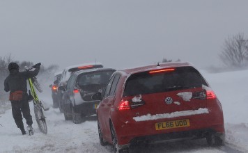 A man pushes his bicycle past cars stuck in the snow in Coalville, Britain on March 18, 2018. Heavy snow continued to hammer the UK. Photo: Reuters
