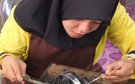 A woman solders a batik printing stamp in Kuala Terengganu, Malaysia. Photo: Keith Mundy