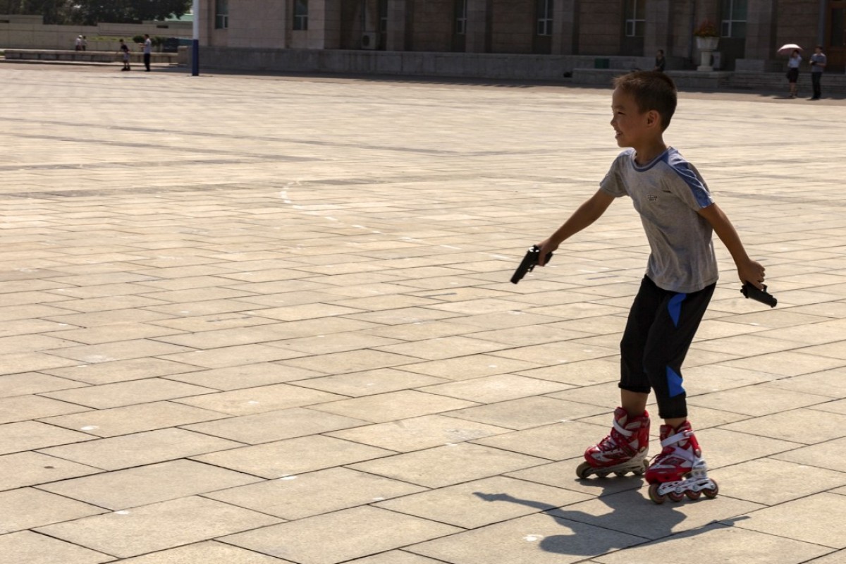 A boy holding toy guns rollerblades in Kim Il Sung Square, which is often used for military parades. The square is bordered by the Taedong River on one side and some of the iconic buildings of Pyongyang, such as the Grand People’s Study House, on the other.